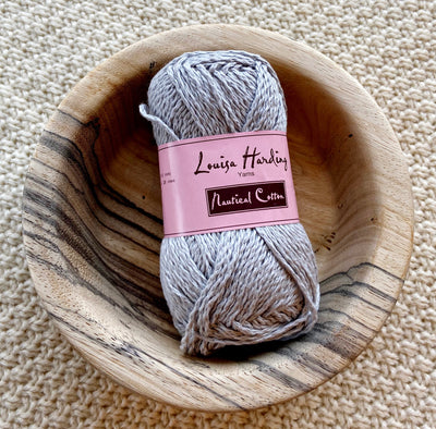 a 50g ball of grey 100% cotton in a wooden bowl on a cream crocheted background