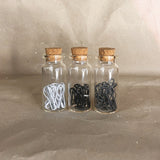 three glass bottles with cork tops white black grey stitch markers inside 