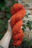 a woman holding a 100g skein of natural dyed bright orange sock yarn 