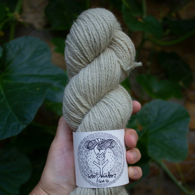 a woman holding a 100g skein of natural dyed white light green sock yarn