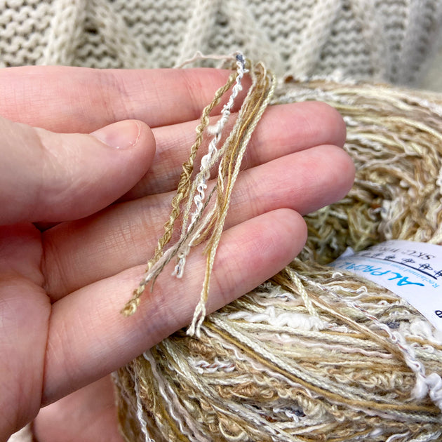 a person hold some strands of white tan multi strand yarn 100g ball