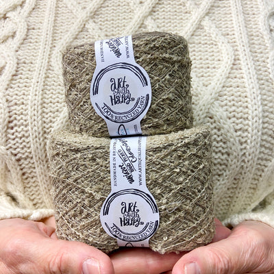 a white woman wearing a cream knitted jumper holding two balls of recycled sock yarn