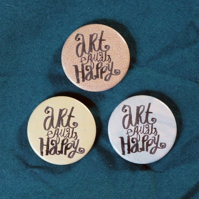 three pin badges gold bronze and white saying art equals happy