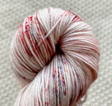 a close up of white red black fingering weight yarn in a 100g skein