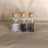 three glass bottles with cork tops white break grey stitch markers in