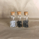 three glass bottles with cork tops white black grey stitch markers in