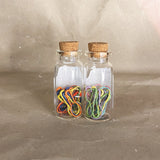 two clear glass bottles with cork tops rainbow pastel red orange green yellow purple green pink stitch markers 