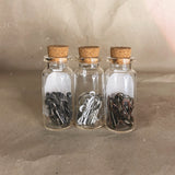 three glass bottles with cork top brown grey red white silver stitch markers 