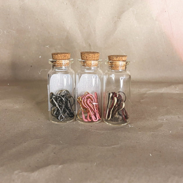 three glass bottles with cork tops white silver gold pink brown white red stitch markers 