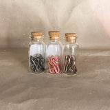 three glass bottles with cork tops white silver gold pink brown white red stitch markers 