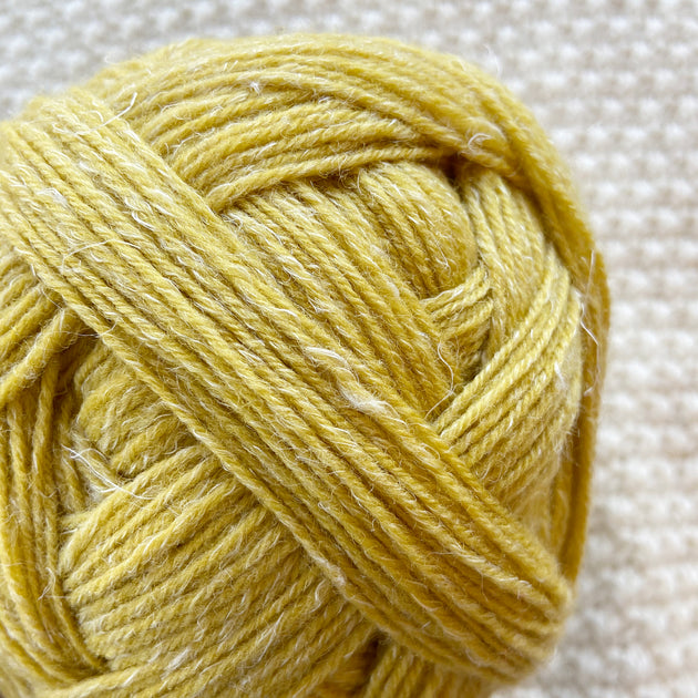 close up of yellow alb lino 100g sock yarn wool and linen on a crocheted white blanket