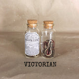 clear small cork bottle with black burgundy red white  stitch markers in