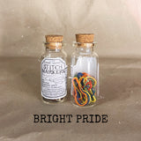 two glass clear bottles with cork lids red orange yellow blue green stitch markers inside  