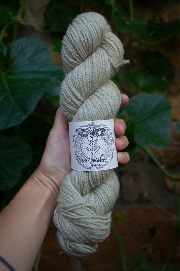 a woman holding a 100g skein of natural dyed white light green sock yarn 