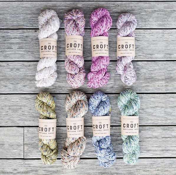 eight skeins of yarn laid out on a wooden background white pink purple green cream blue green 