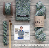 green blue white aran weight skein machine washable for knitting crocheting and weaving a knitted swatch a skein a mini skein a pair of knitting needles a measuring tape a photo of a woman wearing a knitted cardigan made out of the yarn  