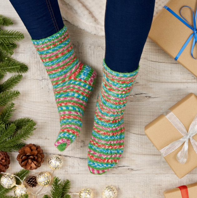 a person wearing blue green white pink red knit socks brown wrapped presents blue leggings pinecones and pine trees 