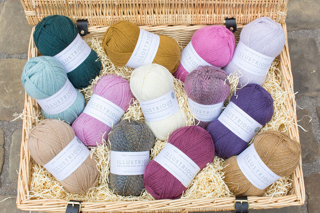 thirteen balls of dk double knit weight yarn in a wicker case green blue cream mustard pink purple white
