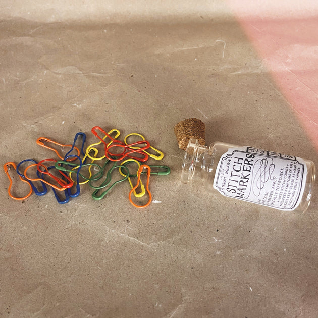 glass bottle led down with cork to the side handful of rainbow  stitch markers spread out