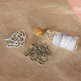 glass bottle led down with cork to the side handful of white stitch markers spread out into groups of whiter and silver
