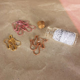 a glass bottle on it's side with the cork top next to it gold pink gold stitch markers 